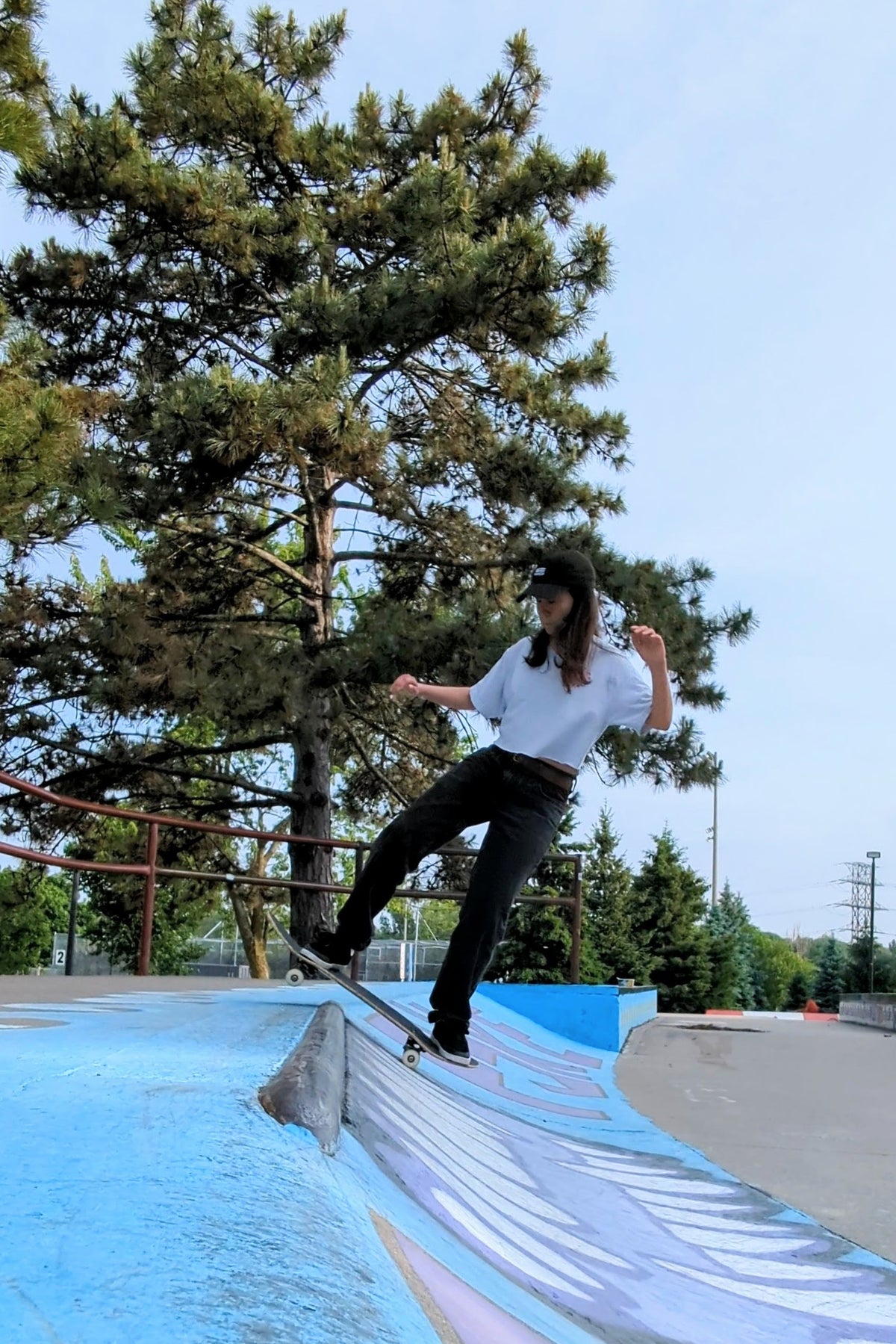 Person skateboarding at a east york skatepark with trees and clear sky in the background